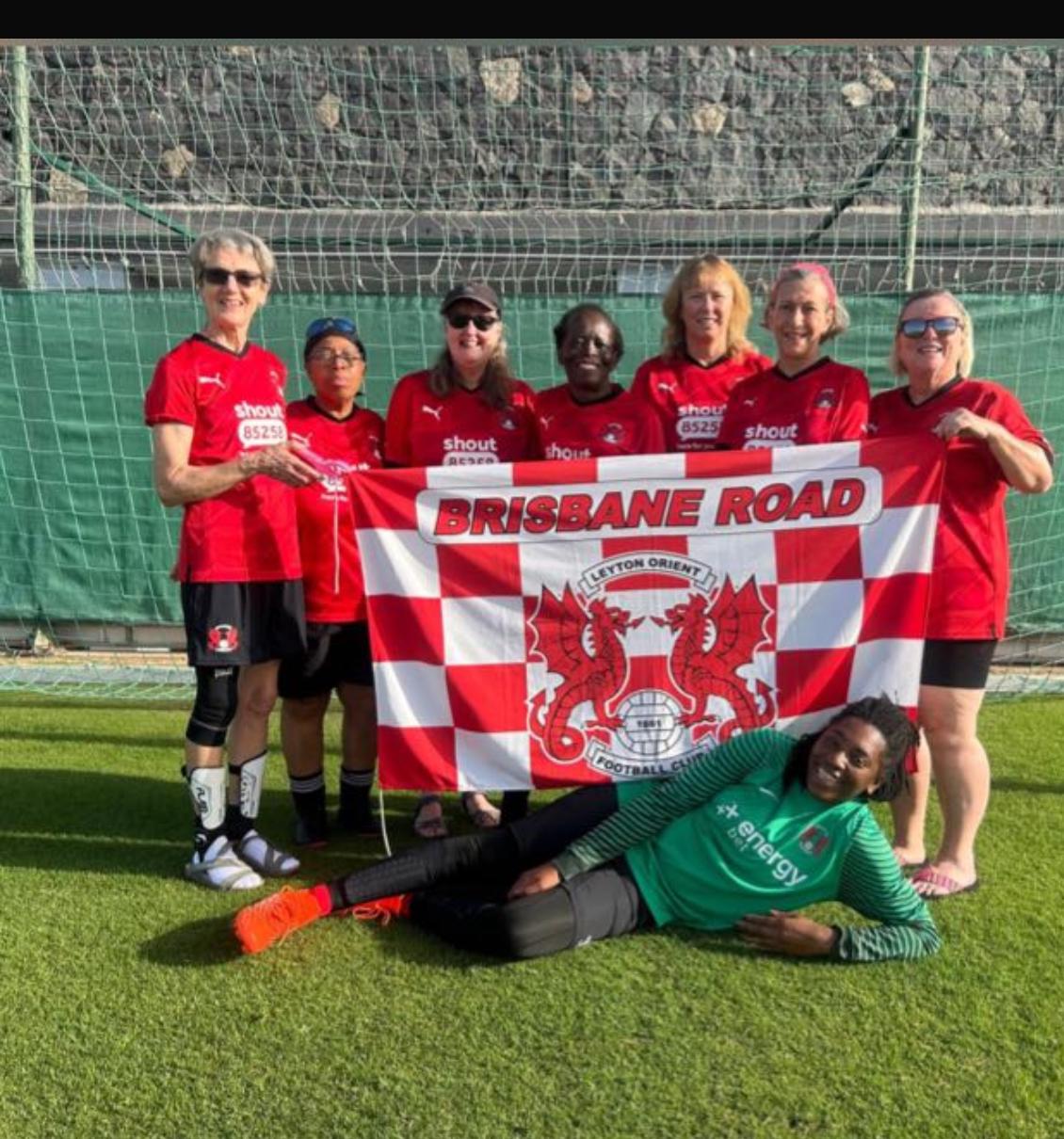 A women's football team holding up their flag while standing and smiling in a football goal