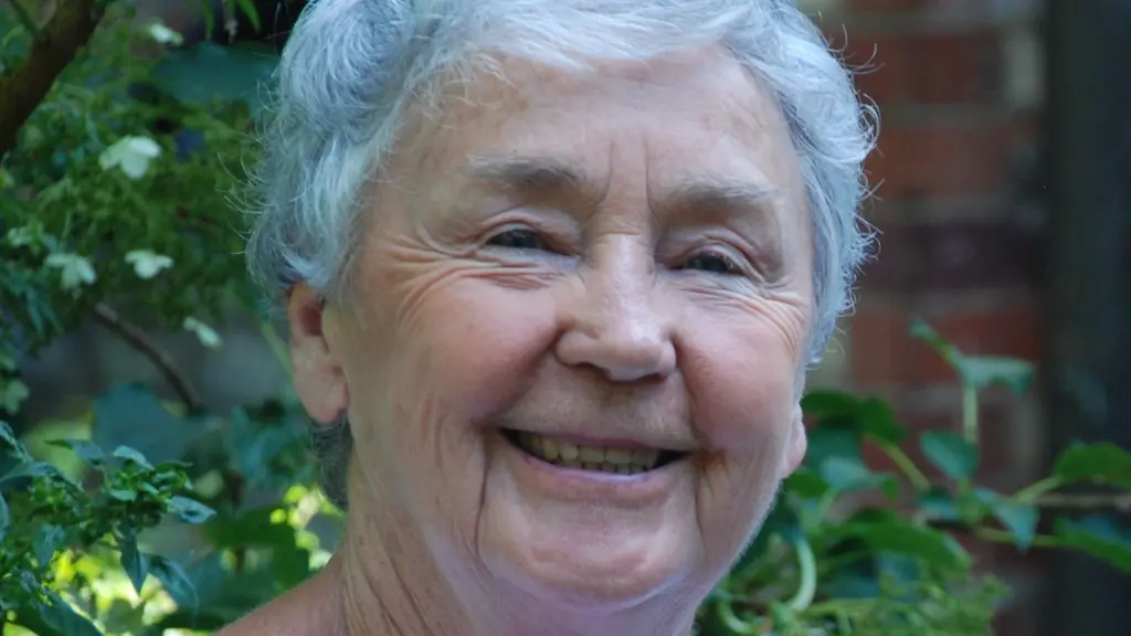 Dolores smiles at the camera with green tree leaves behind her