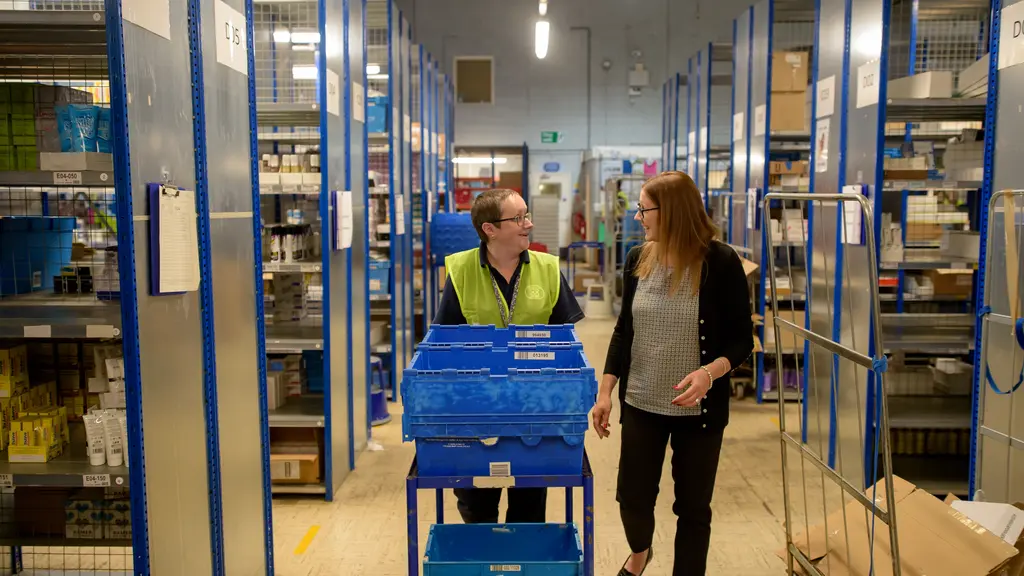 Two women speak while one pushes a trolly in a warehouse