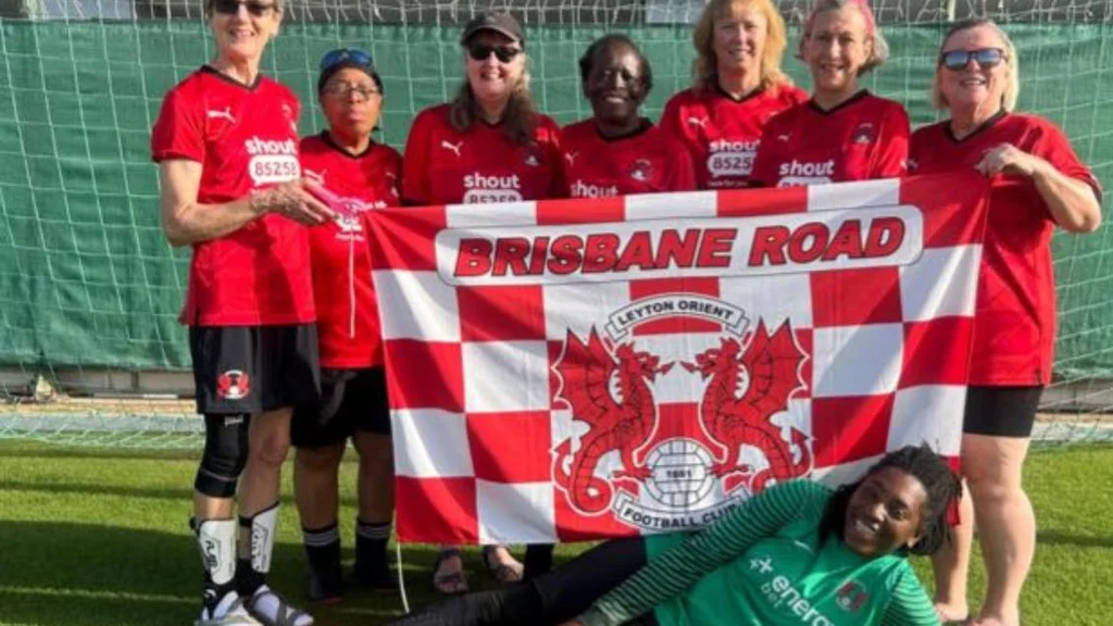 A women's football team holding up their flag while standing and smiling in a football goal