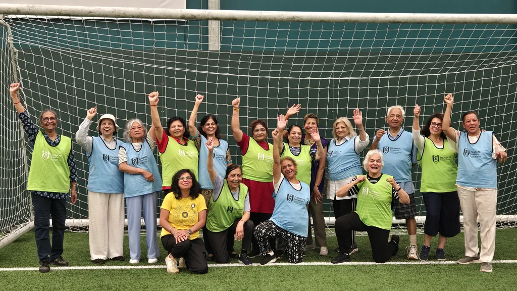A group of older people wearing football vests and smiling with their arms raised as they all stand within a football goal