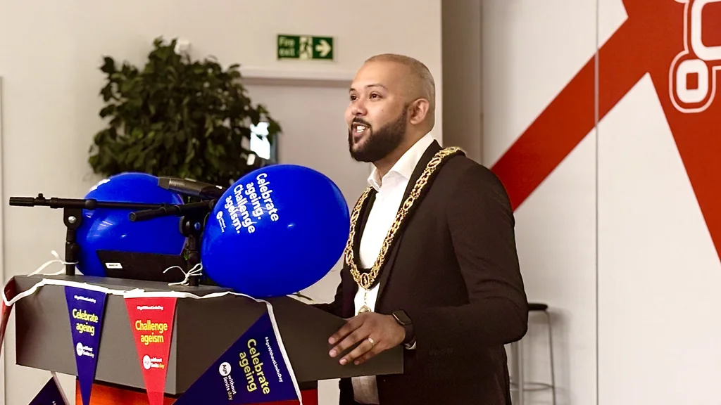 A mayor speaks at a podium decorated in Age Without Limits Day bunting and balloons