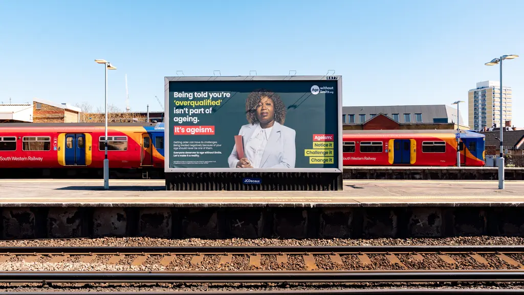 An Age Without Limits advert on a billboard at a train station, with railway tracks in the foreground.