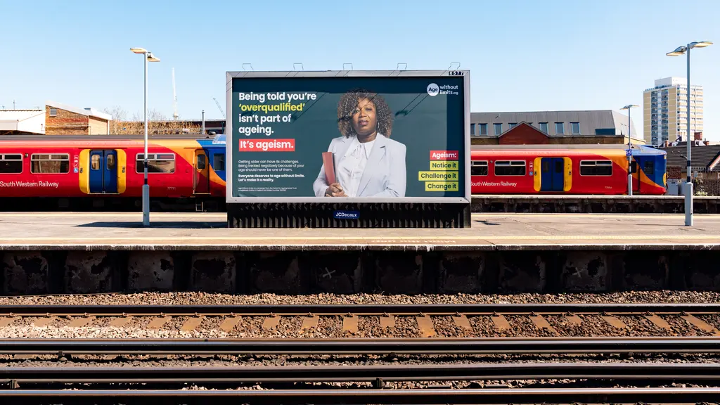 An Age Without Limits advert on a billboard at a train station, with railway tracks in the foreground.
