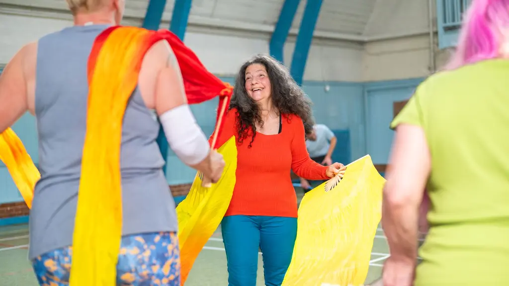 A group of women rehearsing for a circus show and wearing exercise clothes hold bright yellow pieces of flowing fabric