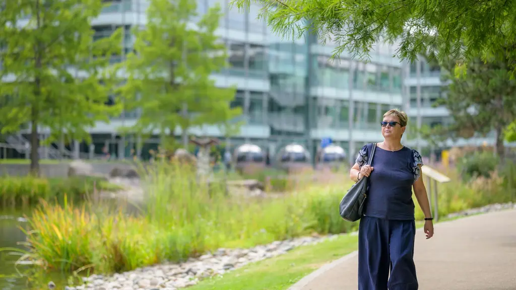 A woman walking outside on a path surrounded by trees and grass