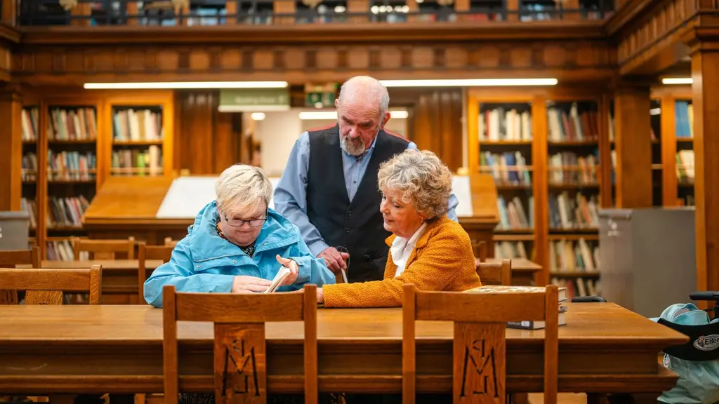 Three older adults look at a book in a library