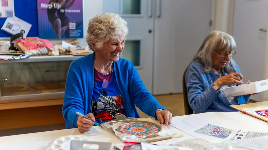 An older woman laughing with her art creation on the table in front of her