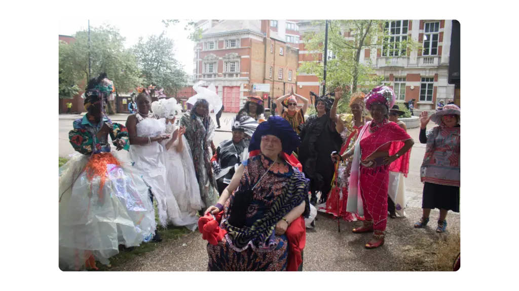 A woman in a wheelchair wears a colourful outfit and behind her is a group of women wearing colourful outfitskground
