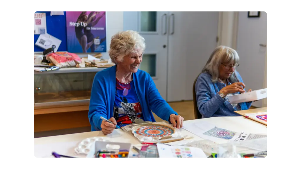 An older woman laughing with her art creation on the table in front of her